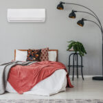 Black stylish lamp in elegant bedroom interior with comfortable double bed, plants, and bedside table, real photo with copy space on the wall