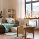 interior, christmas and interior concept - cushioned sofa, coffee table, garland string and candles on window sill in living room of cozy home